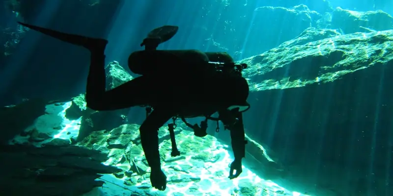 Silhouetted scuba diver in a cenote Chikin ha illuminated by sunbeams