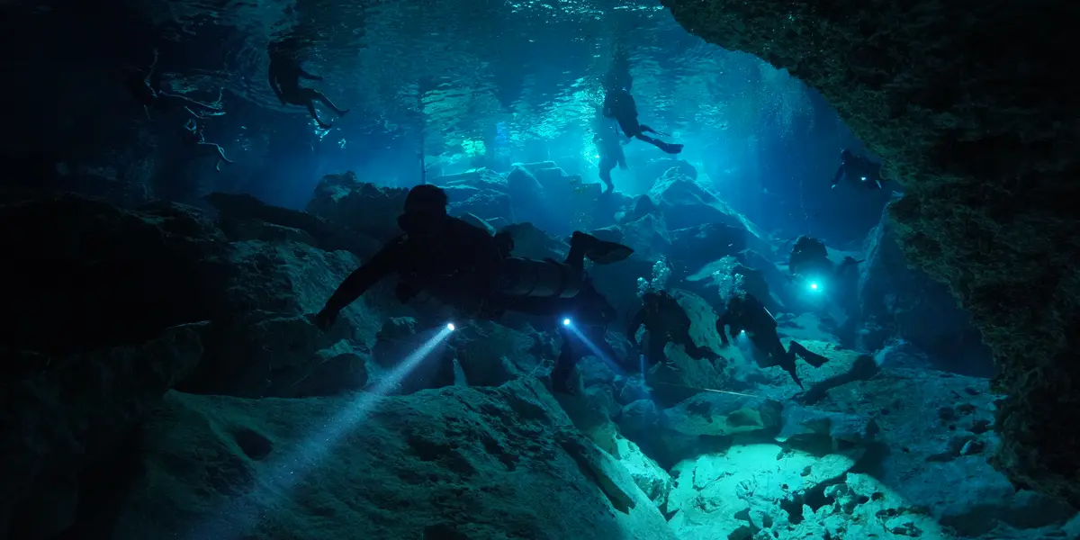 Grupo de buzos certificados explorando la caverna del Cenote Chikin Ha con lámparas 