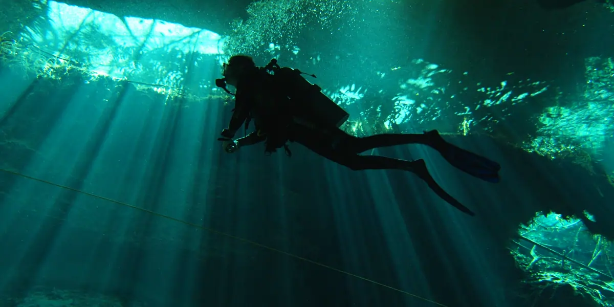 Buzo certificado nadando entre haces de luz natural en el Cenote Chac Mool
